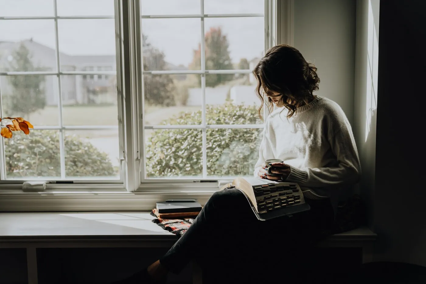 A person sitting by a window holding a mug